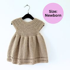 a crocheted dress hanging on a hanger with the text size newborn next to it