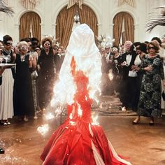 a group of people standing around a red and white dress on fire in the middle of a room