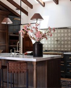 a kitchen island with flowers in a vase on it and two lamps hanging from the ceiling