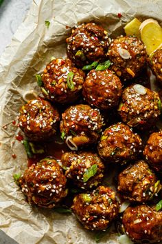 meatballs covered in sesame seeds and garnished with lemon wedges on parchment paper