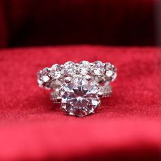 a diamond ring sitting on top of a red velvet cushioned surface with the center stone surrounded by smaller round diamonds