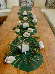 a long wooden table with candles and flowers on the top is decorated with greenery