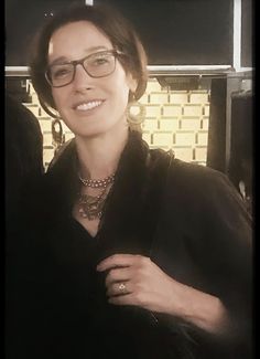 a woman wearing glasses is smiling for the camera while standing in front of a brick wall