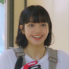 a young woman wearing a white shirt and black suspenders smiles at the camera while standing in front of a window