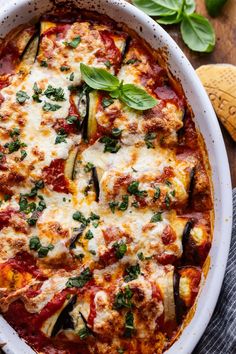 an oval casserole dish with zucchini, cheese and basil on top