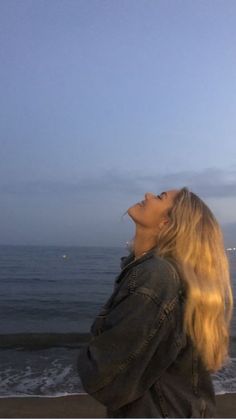 a woman standing on top of a beach next to the ocean looking up into the sky