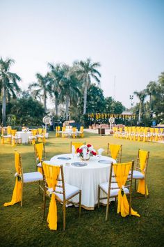 a table set up with yellow and white linens for an outdoor wedding in the grass