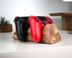 three video game controllers sitting on top of a wooden stand next to a potted plant