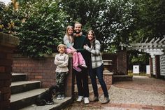 a family poses for a photo in front of some trees and brick steps with their dog