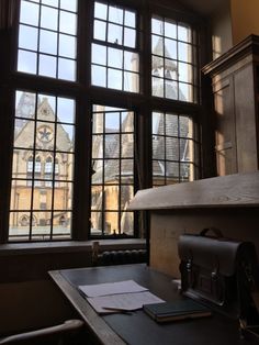 a desk in front of two large windows and a clock tower behind it with papers on it