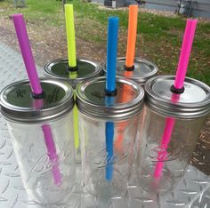 four mason jars with different colored straws and lids on a picnic table in the park