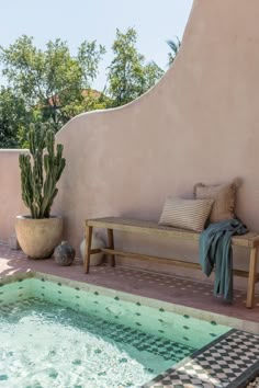 a bench sitting next to a swimming pool with a cactus in the corner and pillows on it