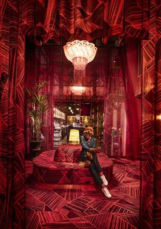 a woman sitting on top of a red couch in a living room filled with furniture