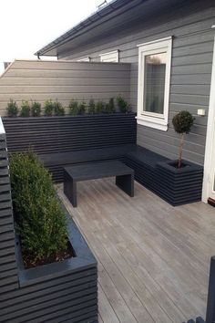 a wooden deck with benches and potted plants next to the house's windows