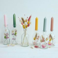 five glass bottles with flowers and candles in them