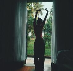 a woman standing in front of a window with her arms up