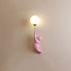 a pink pig lamp hanging from the side of a wall next to a light bulb