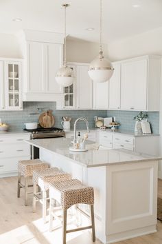 a kitchen with white cabinets and marble counter tops, two stools in front of the island