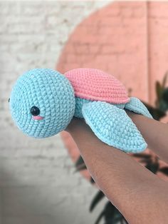 a crocheted blue and pink stuffed animal on someone's arm in front of a brick wall