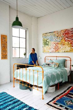 a woman sitting on top of a bed in a room with white walls and blue rugs