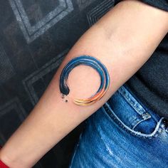 a woman's arm with a tattoo on it that has an orange and blue circle