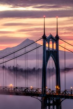 the bridge is surrounded by fog and low lying clouds at dusk, with mountains in the distance