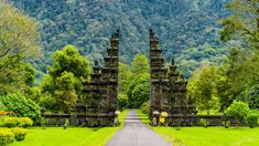 two people are standing in front of an entrance to a lush green park with mountains in the background