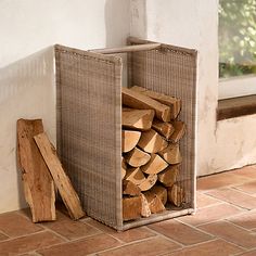 a pile of wood sitting next to a window on top of a brick floor in front of a wall