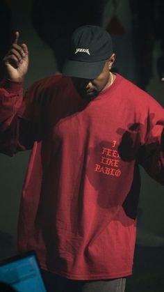 a man in a red shirt and black hat holding his hands up to the side