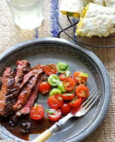 a plate with steak, tomatoes and cucumbers next to a glass of water