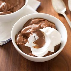 two white bowls filled with chocolate pudding on top of a wooden table next to spoons