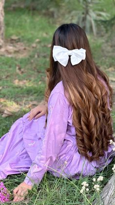 a woman with long hair sitting in the grass wearing a bow tie on her head