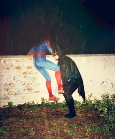 two people dressed up as superman and spider - man standing next to each other in front of a wall