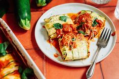 a white plate topped with lasagna covered in sauce and toppings next to a silver fork