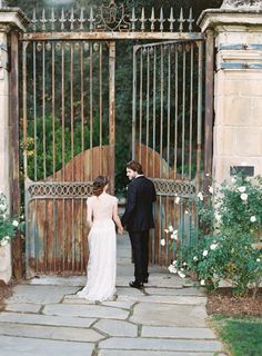 a bride and groom holding hands in front of an iron gate at their wedding reception