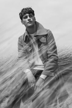 a young man sitting on top of a beach next to the ocean in black and white