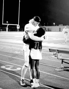 a man and woman hug on the sidelines of a football field at night time