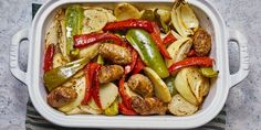 a white casserole dish filled with sausage, peppers and onions on a towel