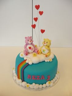 two teddy bears are sitting on top of a rainbow shaped cake with hearts and balloons