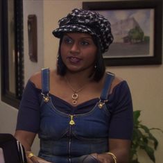 a woman in overalls and a hat is holding a book while looking at the camera