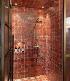 a shower with red tile and gold trim in a bathroom area that looks like it has been tiled