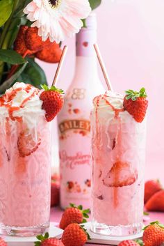 two strawberry milkshakes with whipped cream and strawberries on the rims next to a bottle of booze