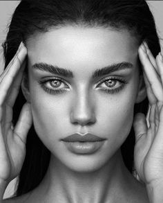 a black and white photo of a woman's face with her hands on her head