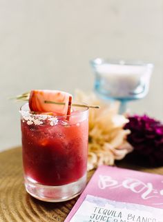 a drink sitting on top of a wooden table next to a menu and flower arrangement