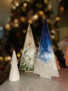 three glass trees sitting on top of a table next to a christmas tree in the background