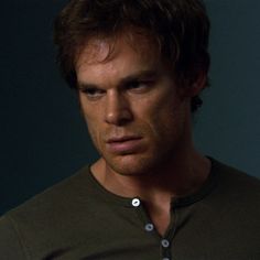 a close up of a person wearing a green shirt and looking at the camera with a serious look on his face