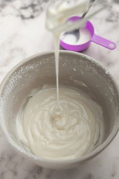 a white bowl filled with cream sitting on top of a counter next to a purple spoon