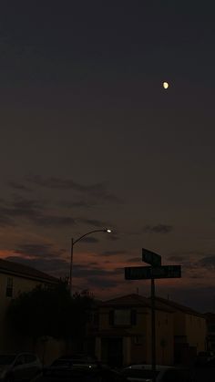 the moon is setting over some houses and street signs