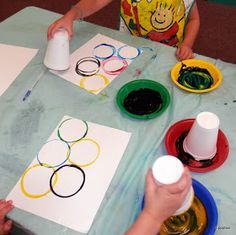 two children are painting on paper at a table with cups and saucers in front of them