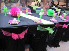 the table is set with black cloths and pink napkins, lime green paper plates